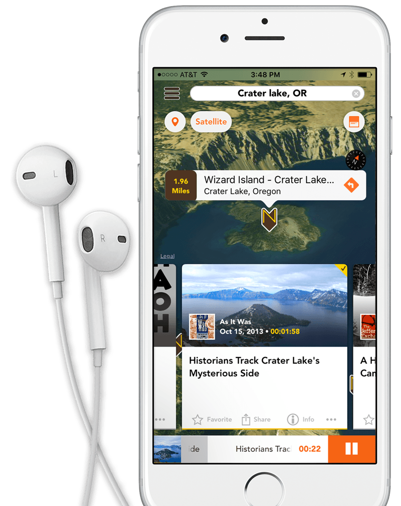 White and sliver iPhone 6 with headphones on the left displays a screen shot of the Nearstory app. On the screen is a 3D map of Crater Lake with focus on Wizard Island. At the top of the screen is a search field that displays Crater Lake, OR. In the middle of teh screen is a Nearstory logo pin and a text cloud with the following: Wizard Island - Crater Lake, Crater Lake, Oregon. 1.96 Miles away. Below Wizard Island at the bottom of the screen is a square story card displaying the playing audio story. On the card is a picture of Wizard Island and Crater Lake, Oregon. Logo for podcast (As It Was) sits in the lower left hand corner. To the right of the podcast logo is the podcast producer title (As It Was). Below the producer title is a publish date of October 15, 2013. to the right of the publish date is a runing time of 1 minute and 58 seconds. Just below the crater lake image in the story card is the title of the podcast episode, 'Historians Track Crater Lakes Mysterious Side. At the bottom of the card is four links, Favorite, Share, Info and an Elipse. Below the audio story card sitting at the bottom of the iPhone screen is a audio player displaying the audio story image to the right with a long strip of white with a gray status bar the audio track srolling through the palyer and the current track time with a large rectangular orange pause button on the right. Behind the iphone is a beautiful picture of Crater Lake National Park. The image fills the entire width of the screen. Snow lightly covers the ground and the sun is bright and dramatic. It looks like it was an early morning or dusk shot. The temperature looks crisp. The water is a deep blue, not a dark blue but not light either. Pine trees can be seen on the left side of the image. In the middle of the shot is Wizard Island looking like a small volcano.